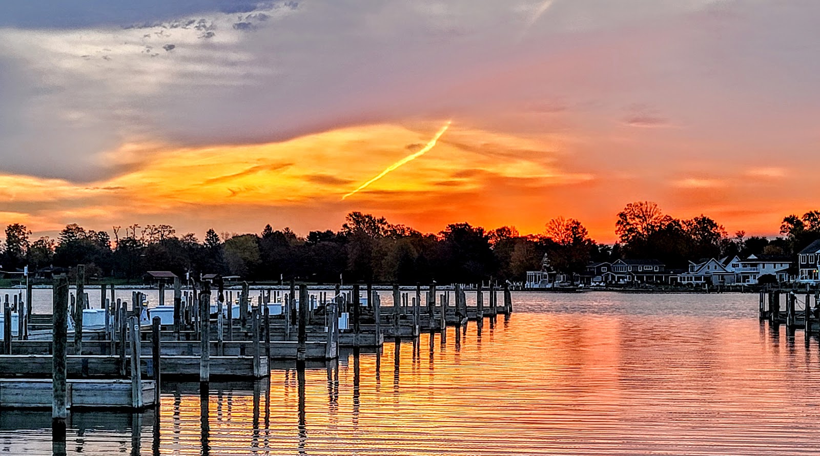 An orange and violet sunset over flat water, a long line of empty timber docks running out from the near shore and the far bank reduced to a dark silhouette.