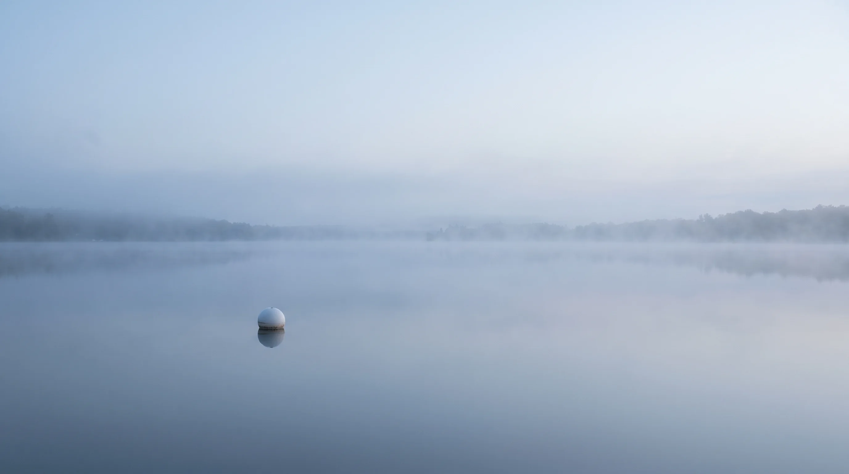 A single buoy on a calm inland lake at dawn