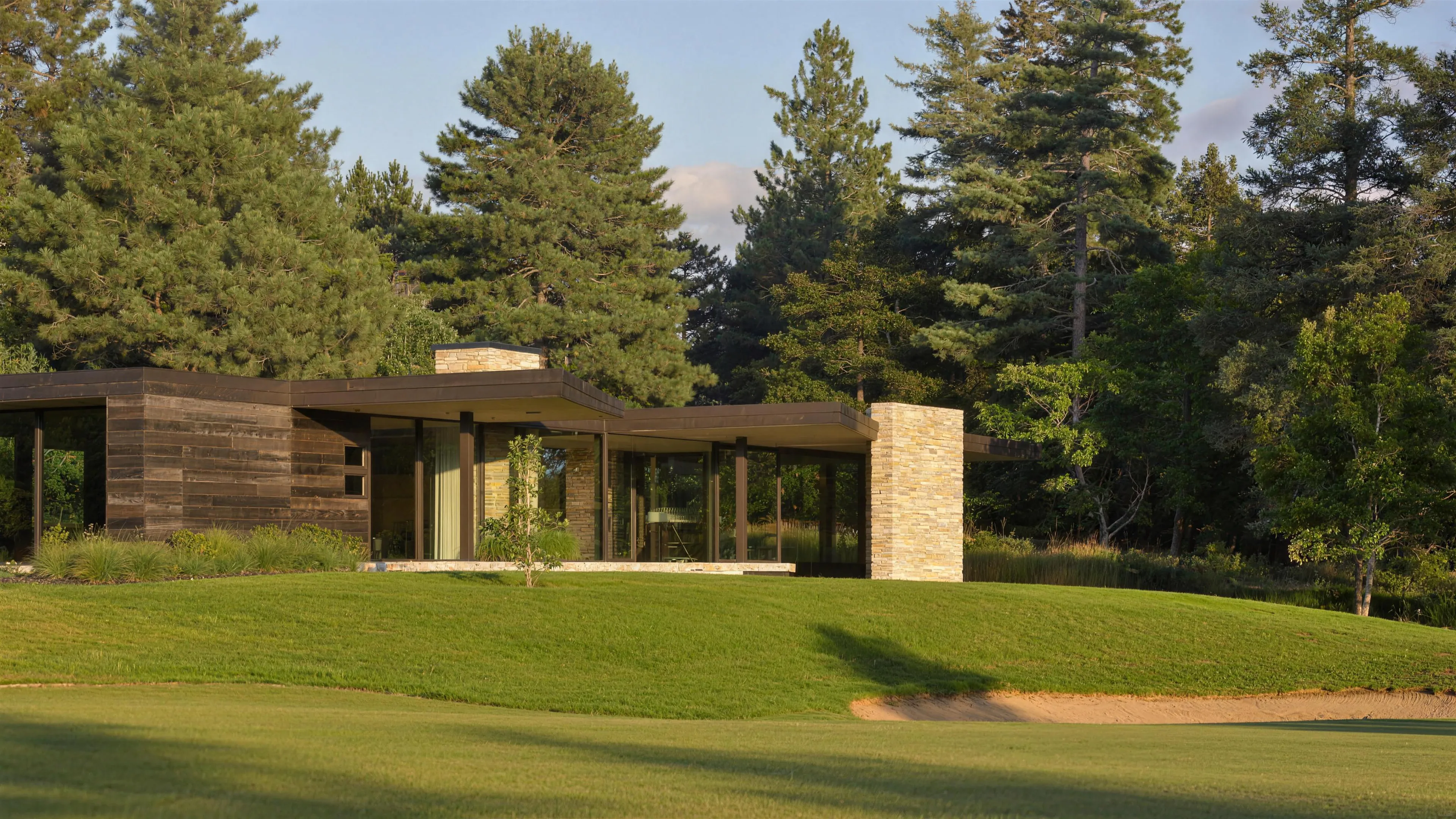 A low modern house standing along a mown fairway under late-afternoon light